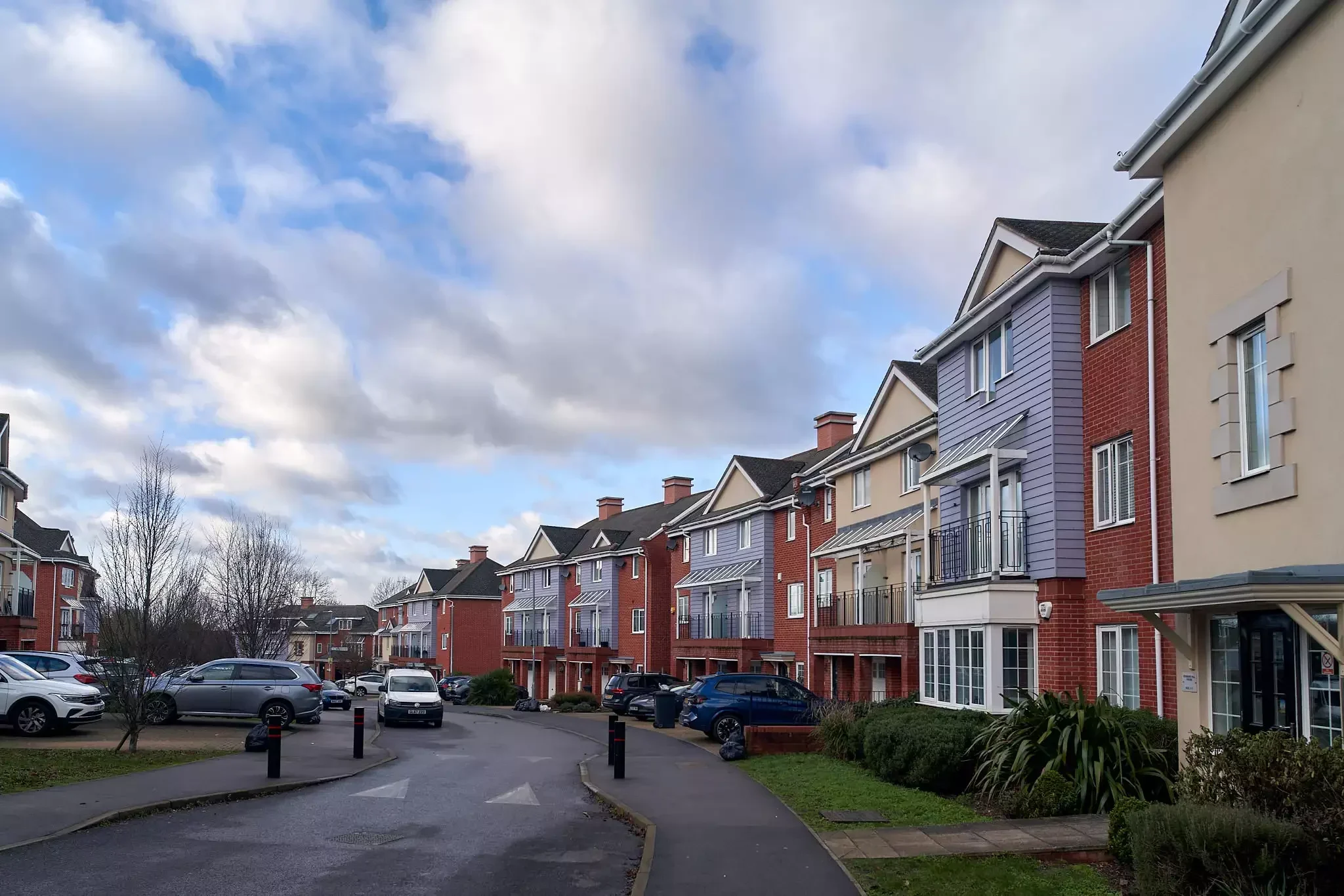Row of colourful modern townhouses with parked cars along a quiet residential street