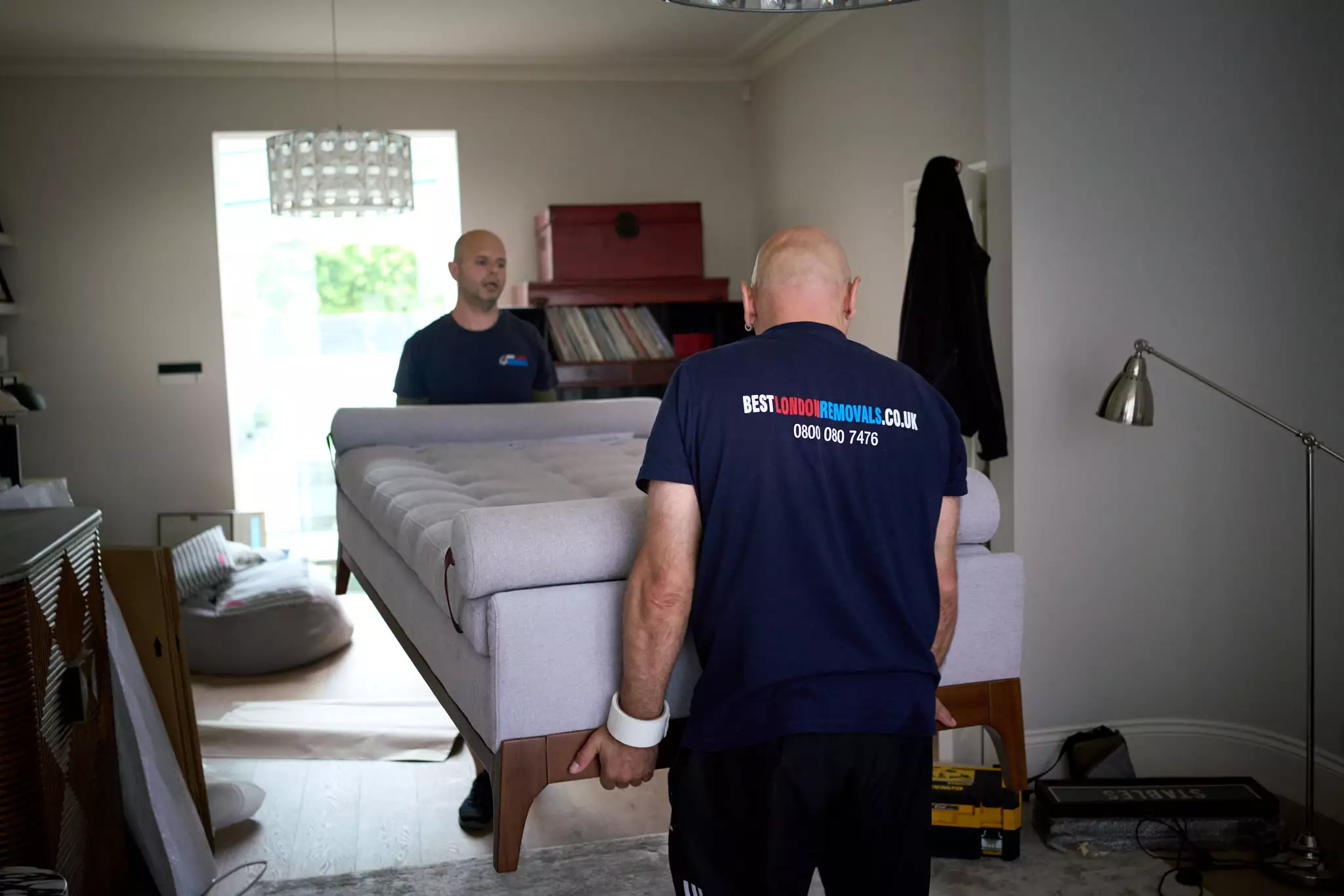 Best London Removals staff lifting a light grey sofa indoors during a home move