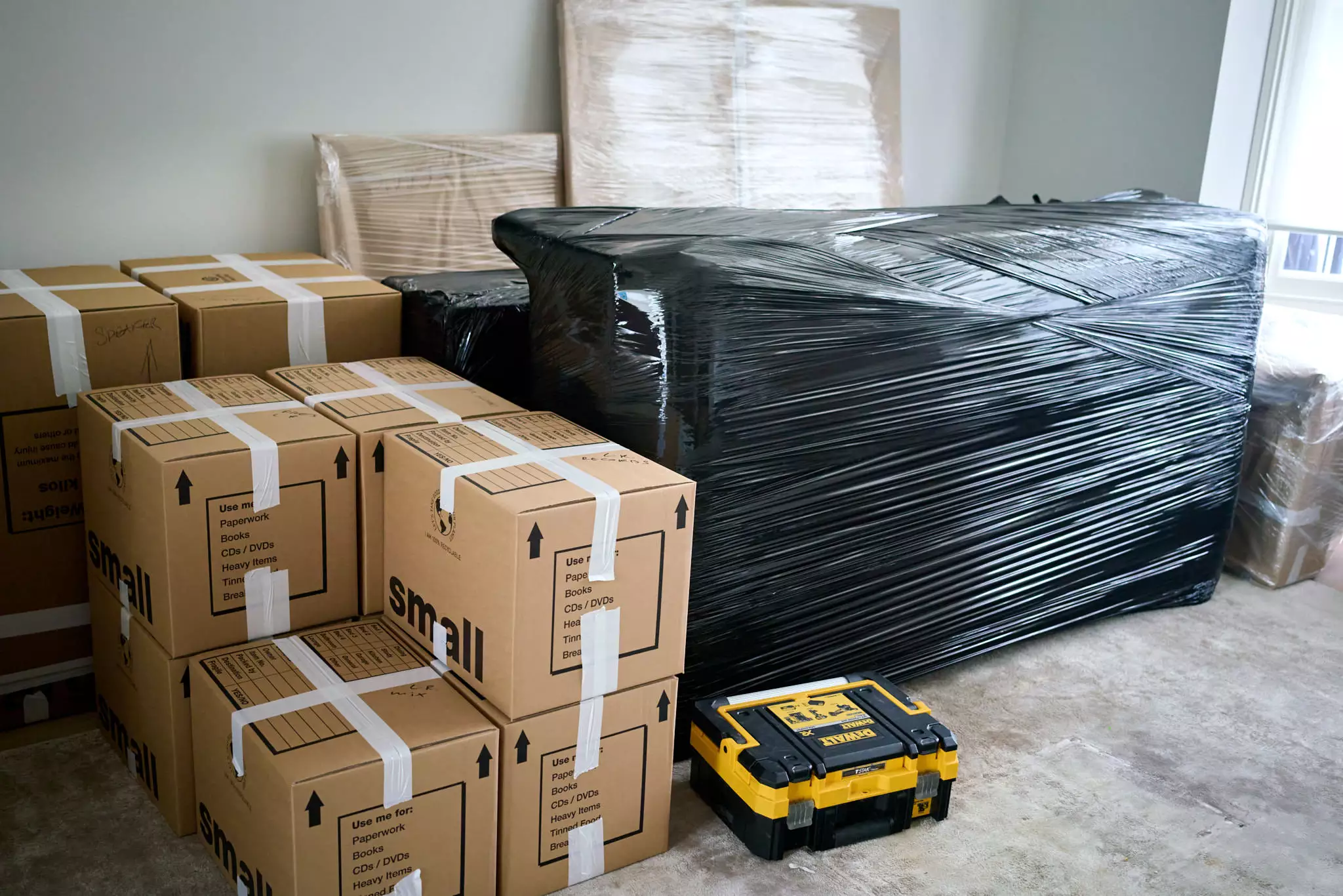 Boxes clearly labelled and secured, alongside large furniture wrapped in black plastic film—showcasing professional packing by Best London Removals