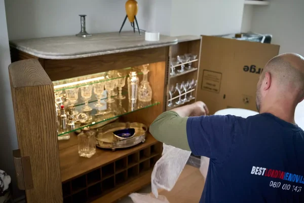 Packing service London- Mover packing glassware and fragile items from a cabinet using protective materials. How to choose the best removal company in London