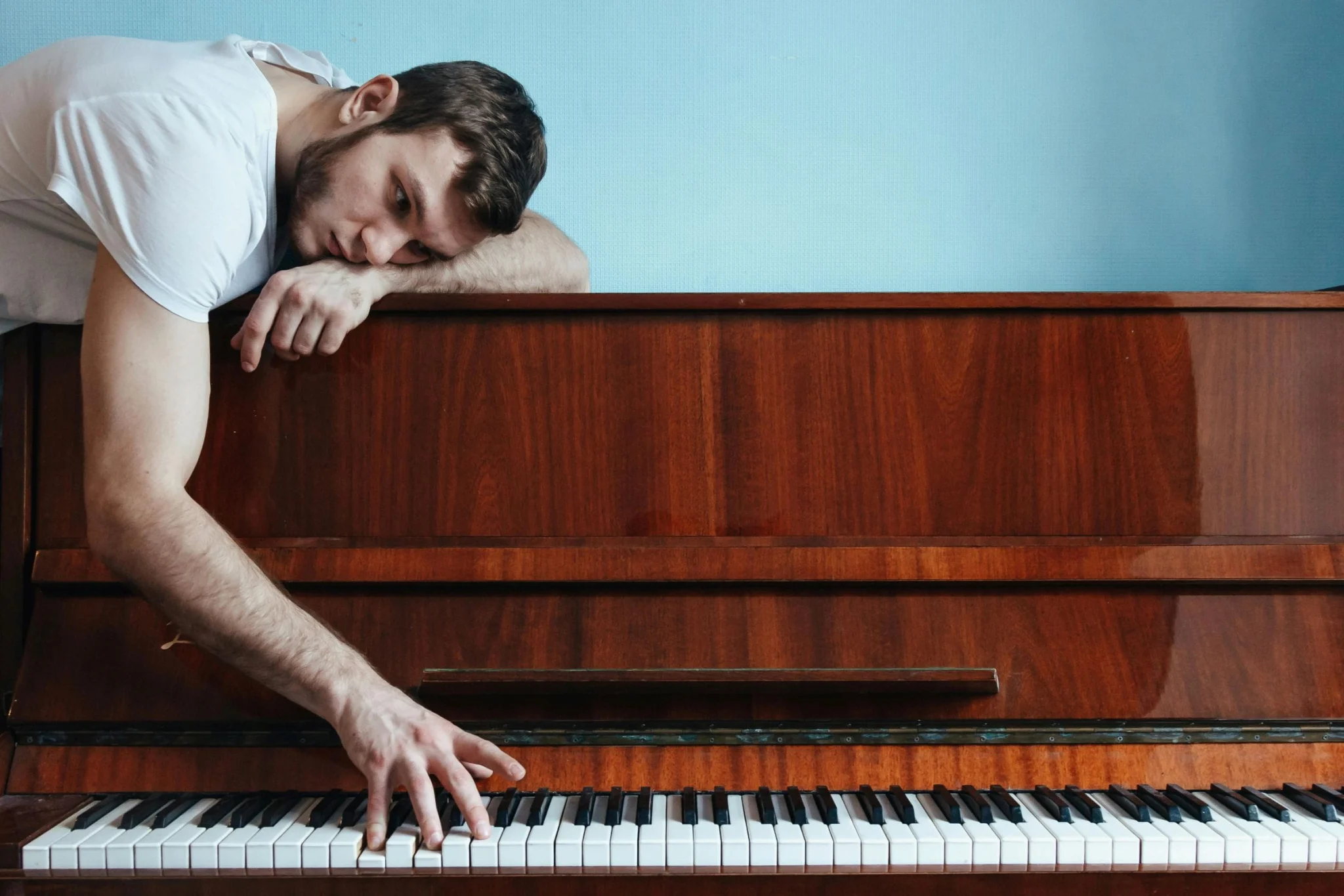 Man resting on upright piano, symbolising emotional care – specialist piano movers in London