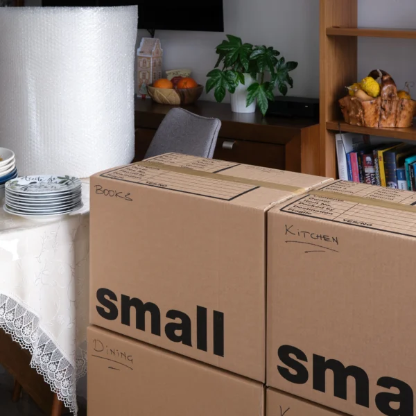 Labelled small moving boxes packed with kitchen, books, and dining items next to bubble wrap and plates