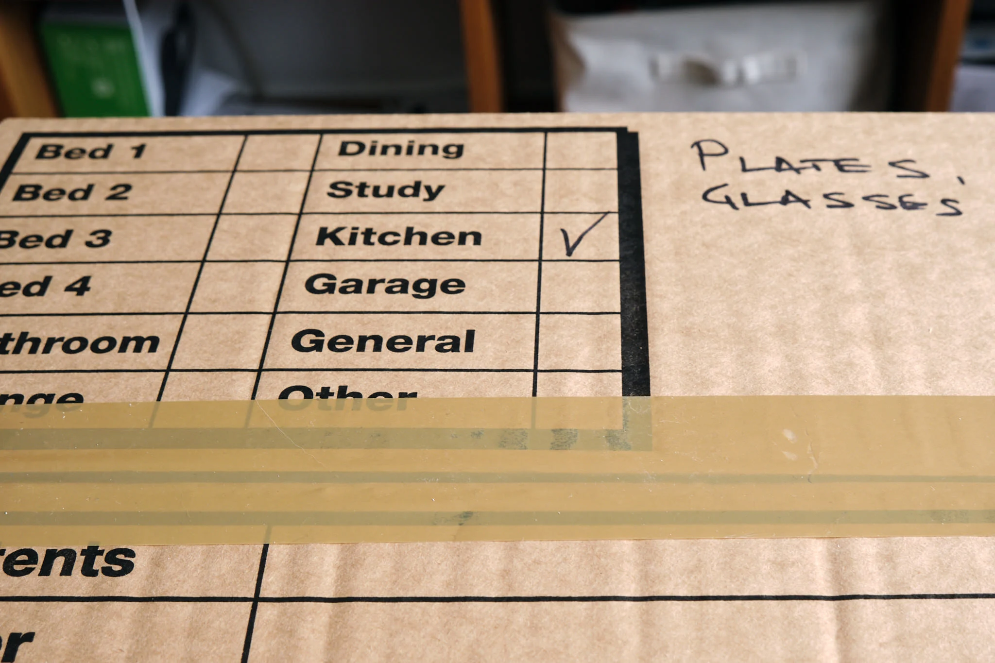 Close-up of a labelled moving box marked for kitchen items, including plates and glasses