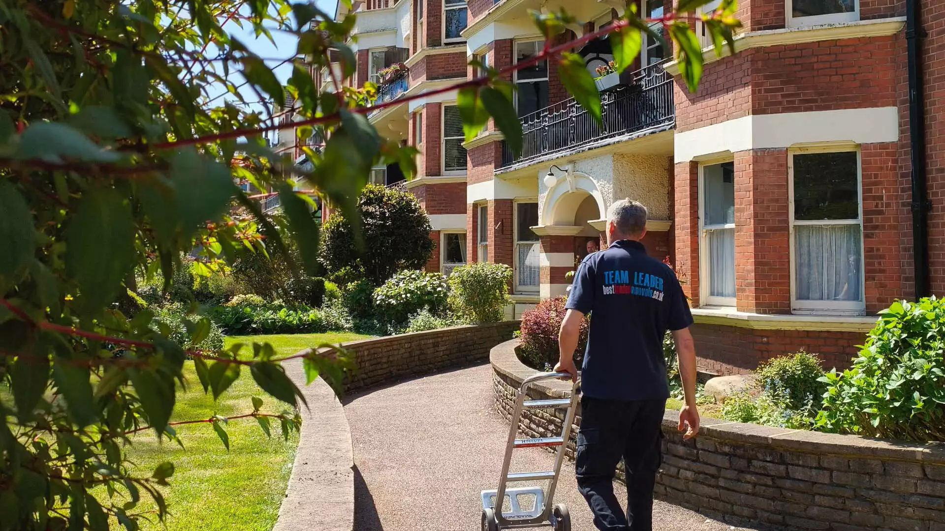 Removal team leader wheeling trolley to Victorian apartment building
