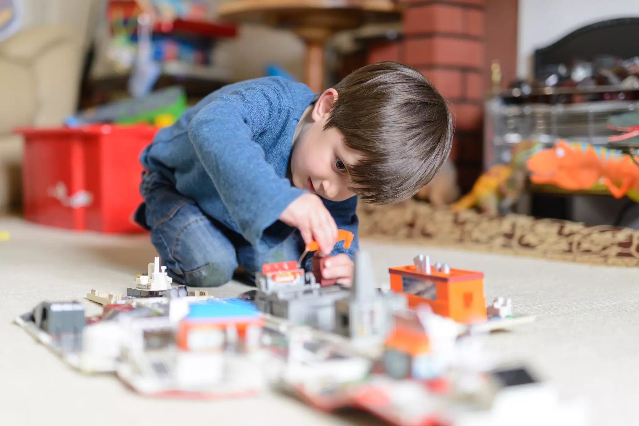 Young boy crouching on the floor and playing with model toy buildings and vehicles
