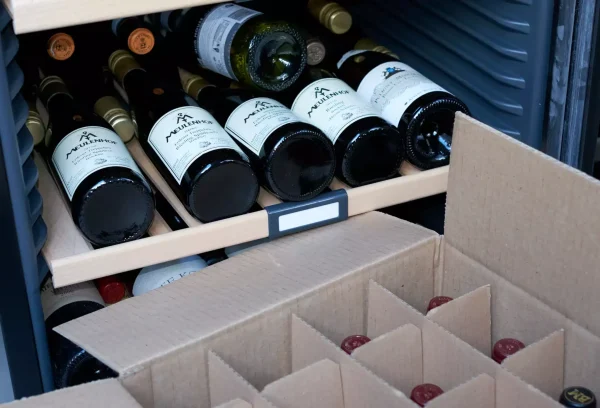 Close-up of fine wine bottles stored in a wine fridge and being packed into a protective box for safe transport during a move