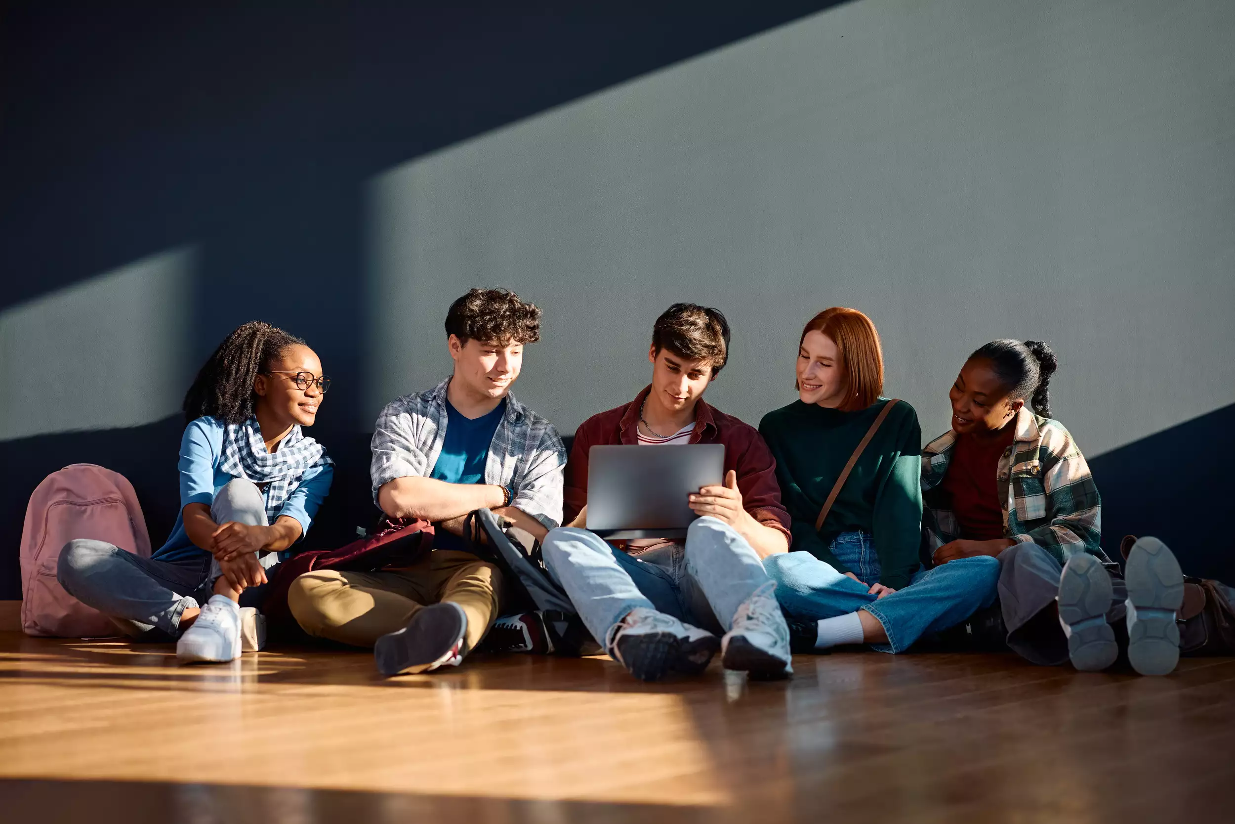 University students sitting on the floor with backpacks and a laptop, smiling and relaxed—ideal for student relocation services.