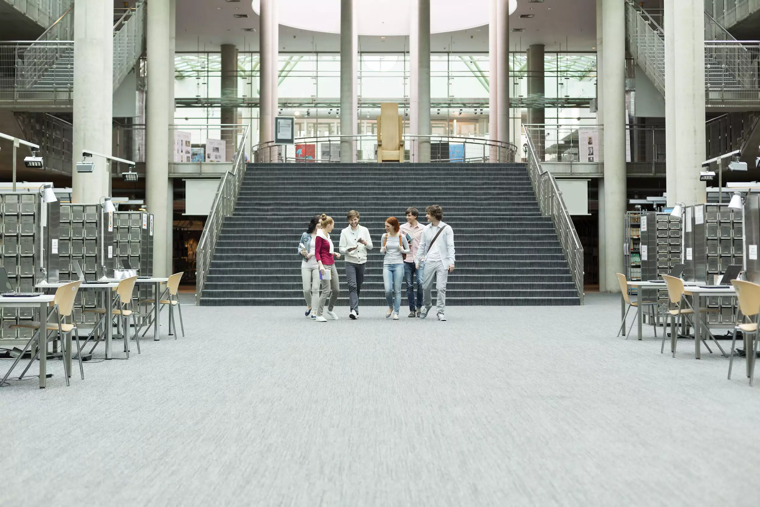 Students walking together inside a large modern university library, symbolising the start of student life.