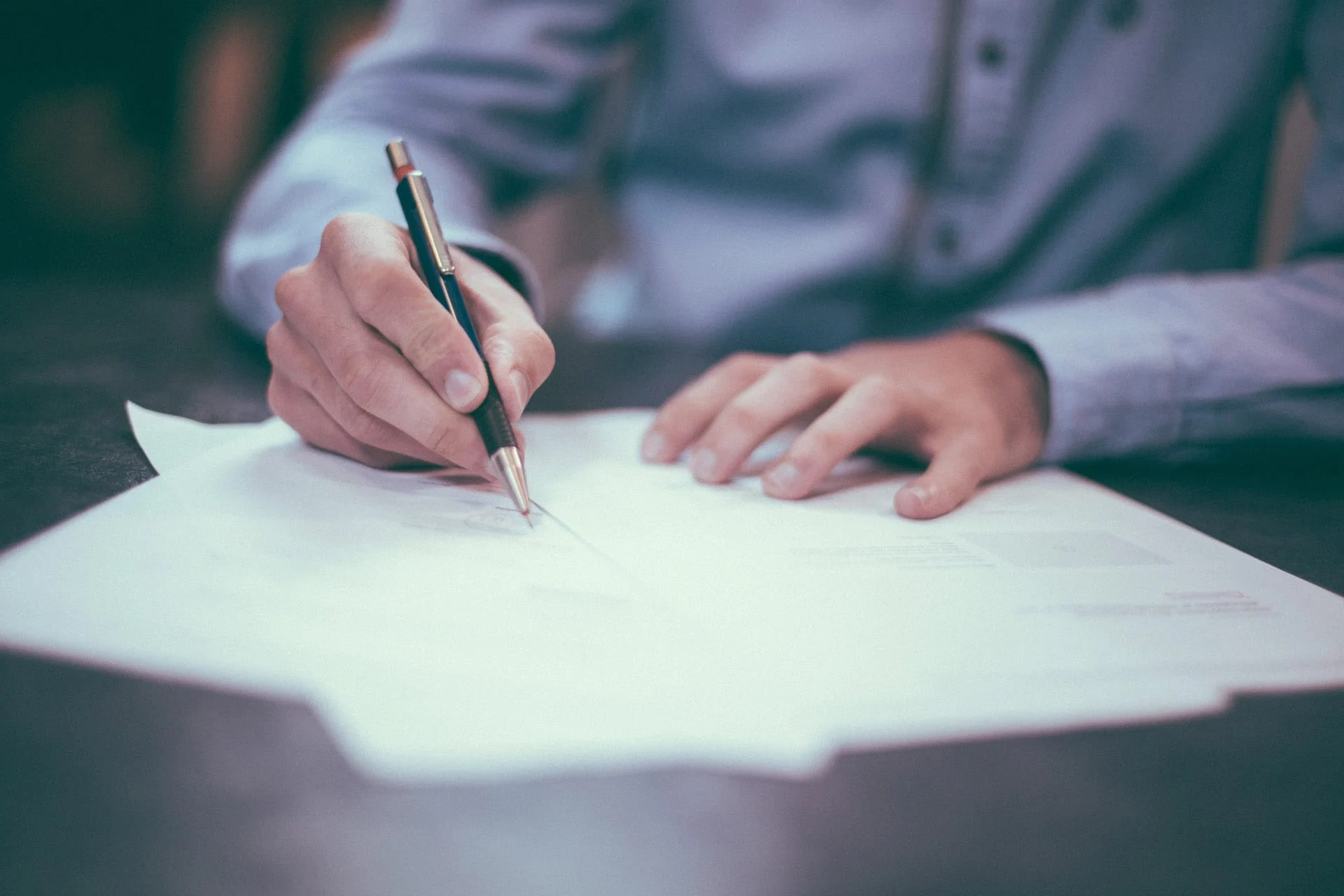 Close-up of a person signing a moving contract with a pen on a desk