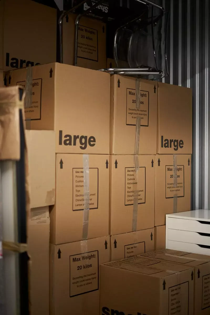 Stacked large moving boxes inside a secure storage unit with chairs placed on top