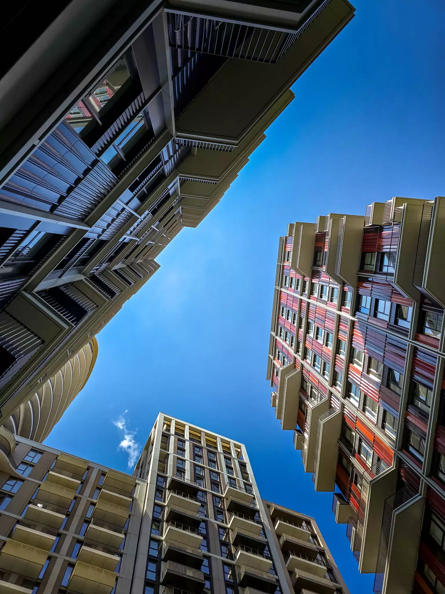 Looking up at high-rise modern flats in London with balconies and a blue sky above