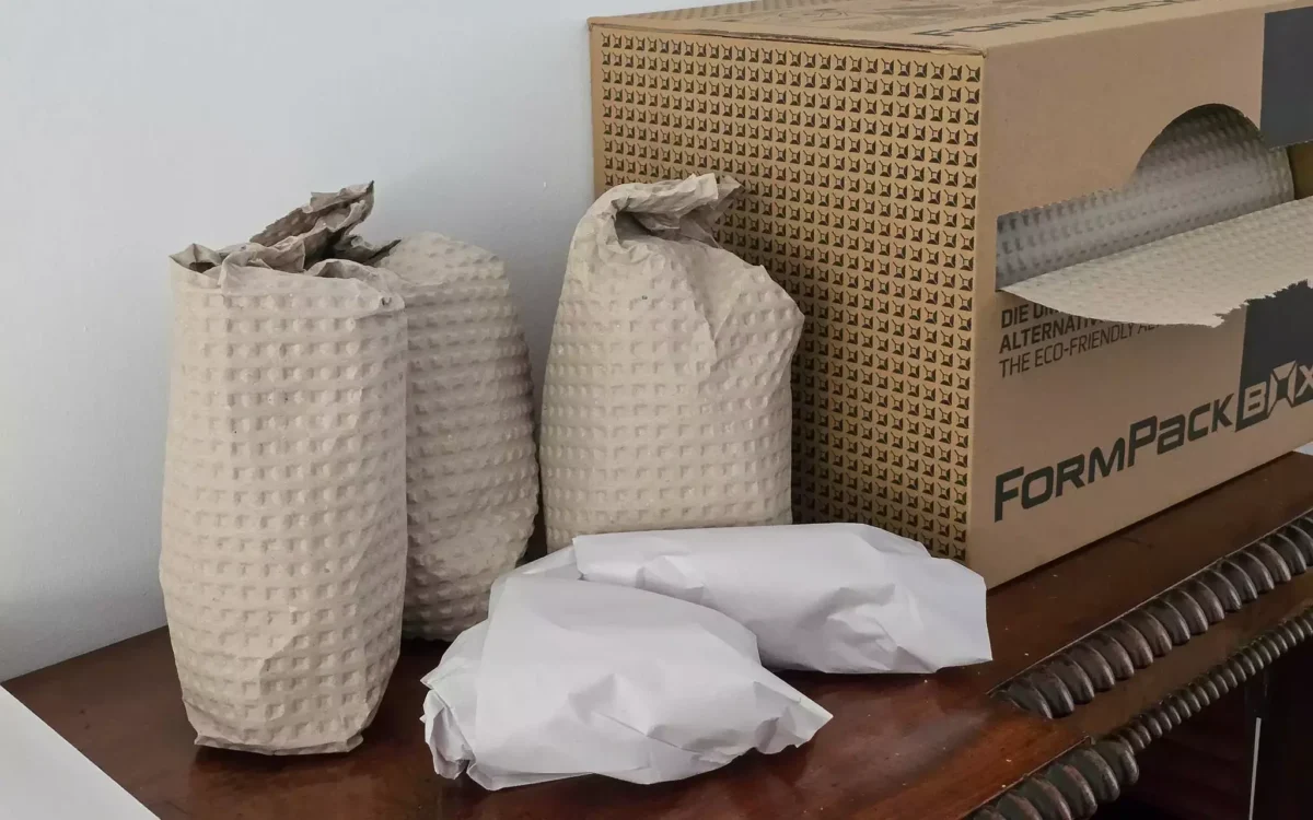 Ornaments wrapped in protective FormPack and paper, placed beside an open eco-wrap dispenser box.