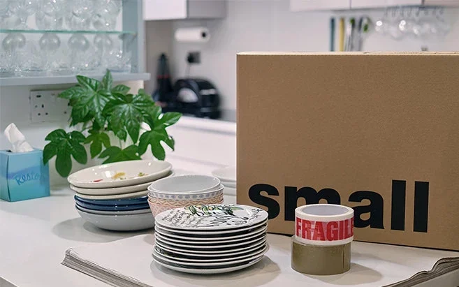 Plates, bowls and a small moving box with fragile tape on a kitchen worktop, ready for packing