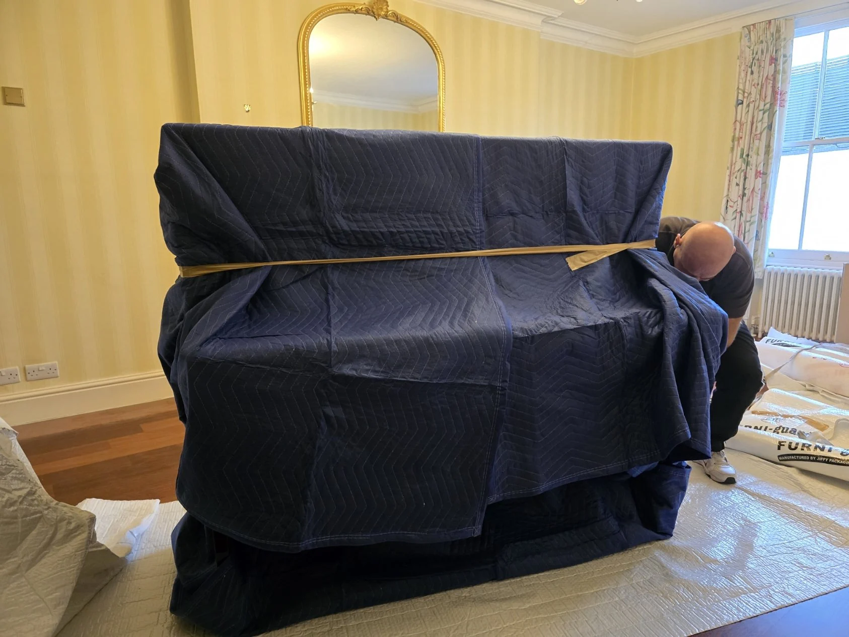 Man wrapping large upright piano in protective moving blankets