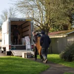 Two movers carrying a chest of drawers from a removal van during a house move in a suburban neighbourhood