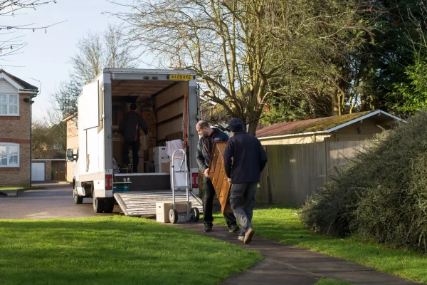 Two movers carrying a chest of drawers from a removal van during a house move in a suburban neighbourhood