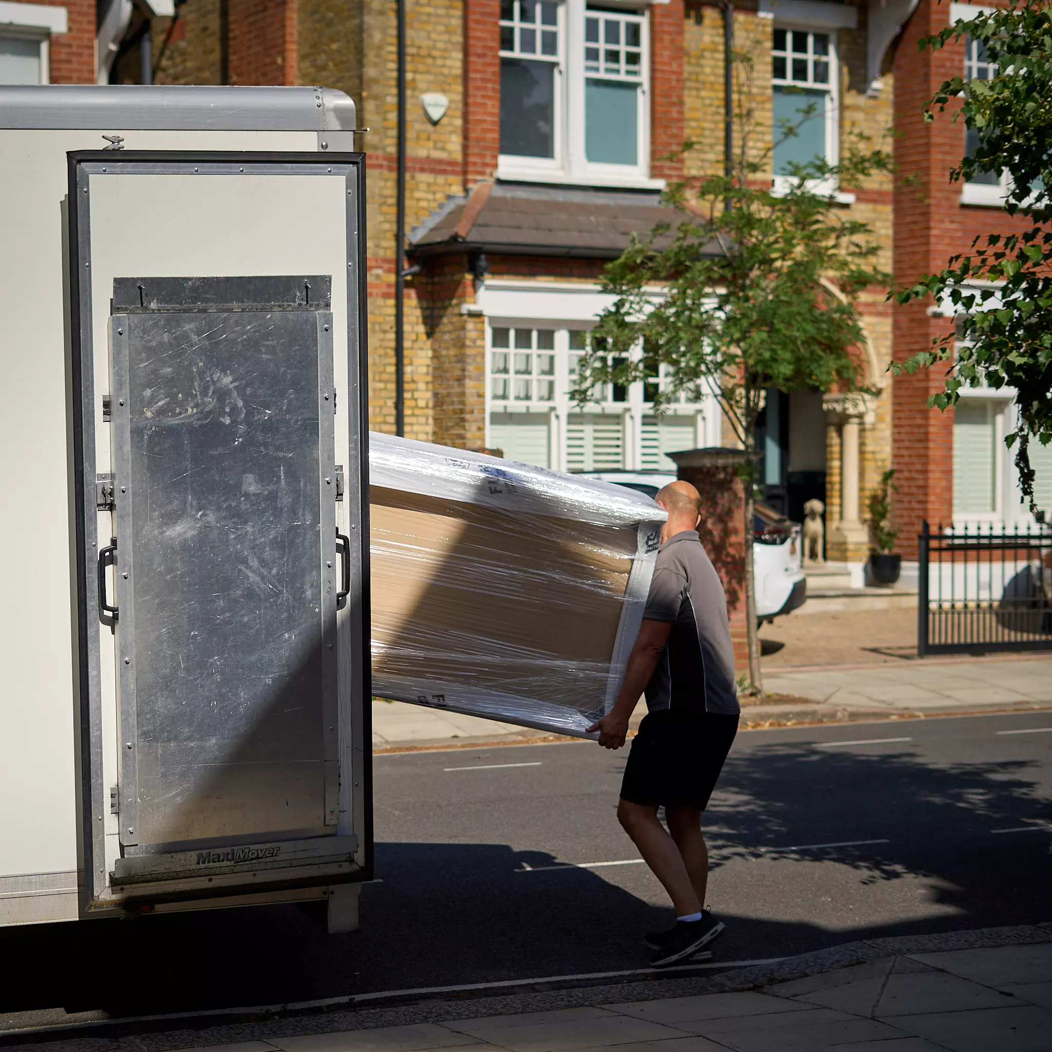 Mover loading wrapped furniture into van outside a home in Ealing during a house move.