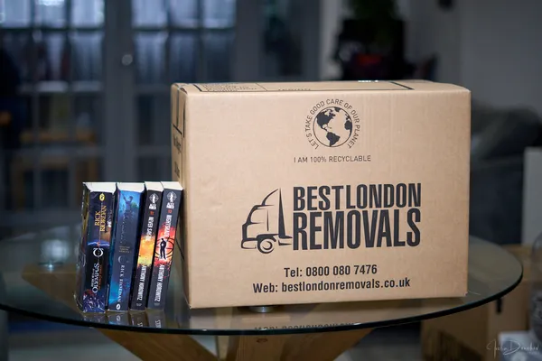 Best London Removals branded moving box on a glass table next to a stack of books