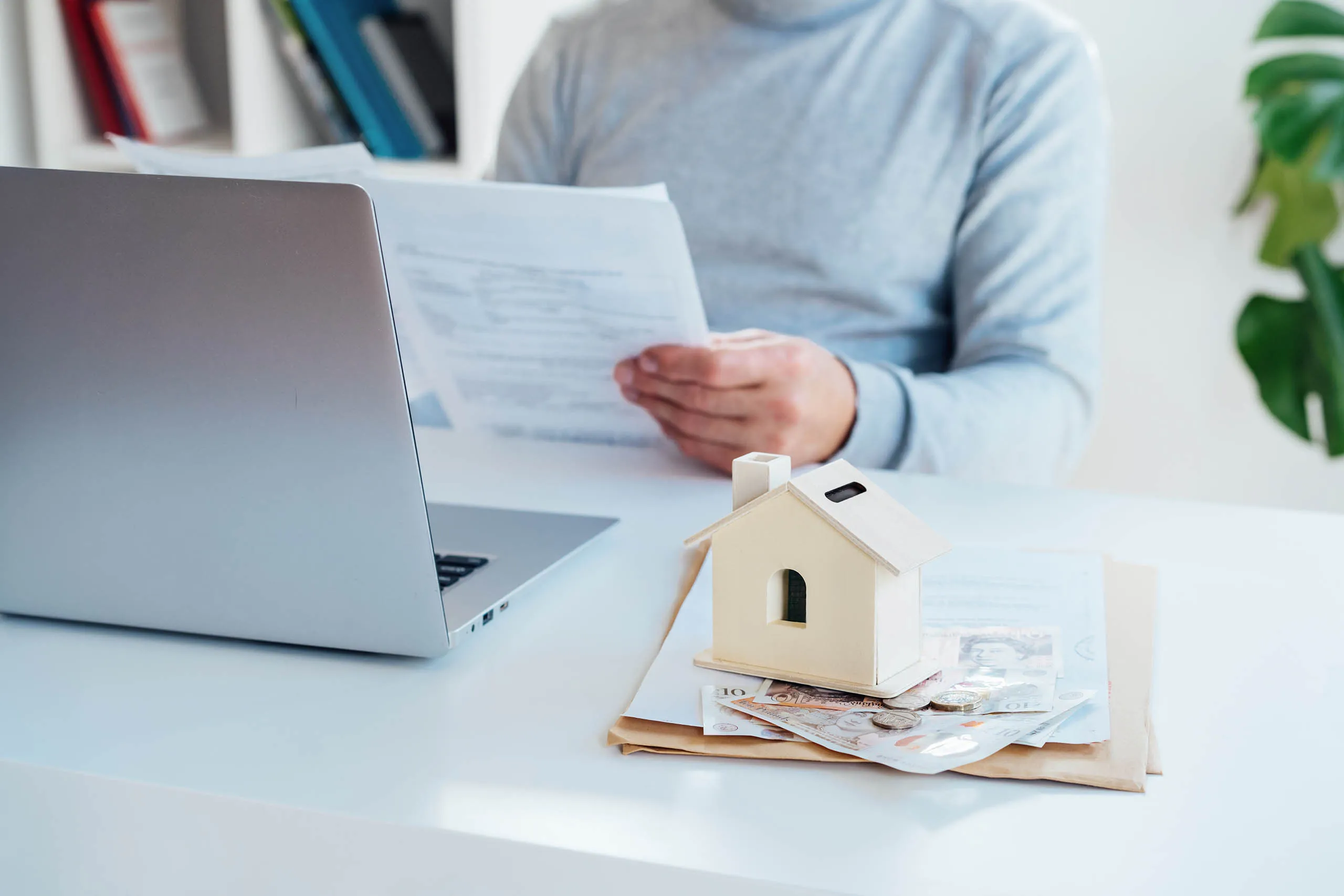 Person reviewing mortgage documents beside model house and cash