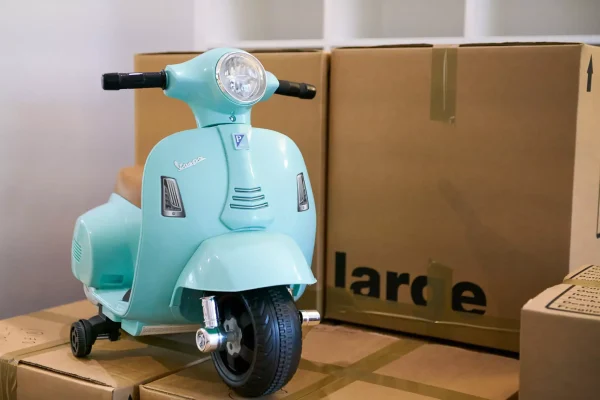 Blue toy Vespa scooter placed on top of taped cardboard moving boxes